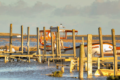 Boats beside the jetty at Morston Quay with harbour posts and calm water