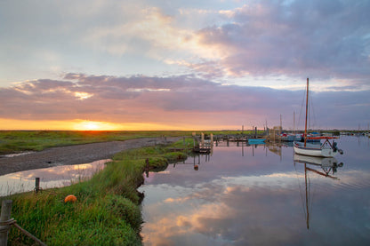 Sunset glow over Morston Quay creek with reflections and boats in the distance