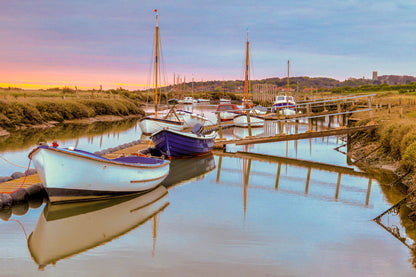 Wooden gangway leading to boats at Morston Quay with calm water reflections