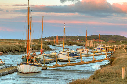 Boats moored by the pontoon at Morston Quay with evening sky over the marsh