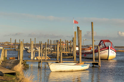 Golden light over Morston Quay with harbour posts, boats and soft reflections